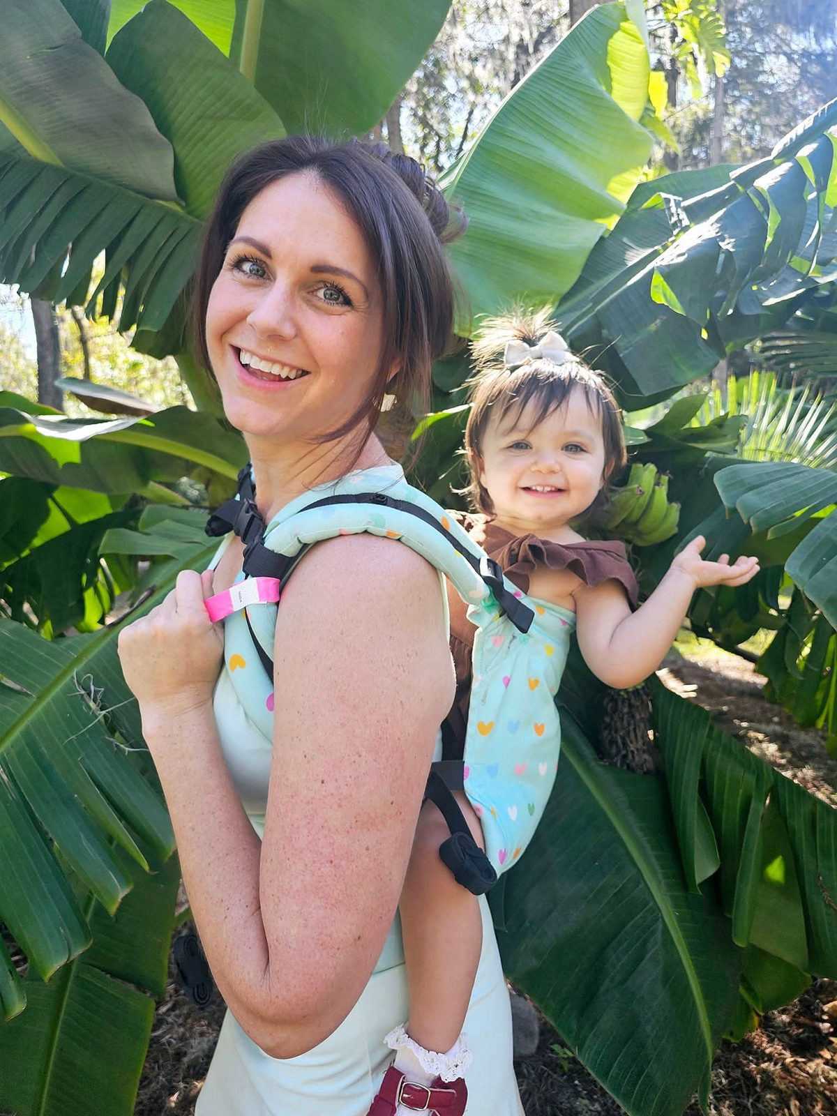 Sarah carrying her daughter on her back among banana leaves