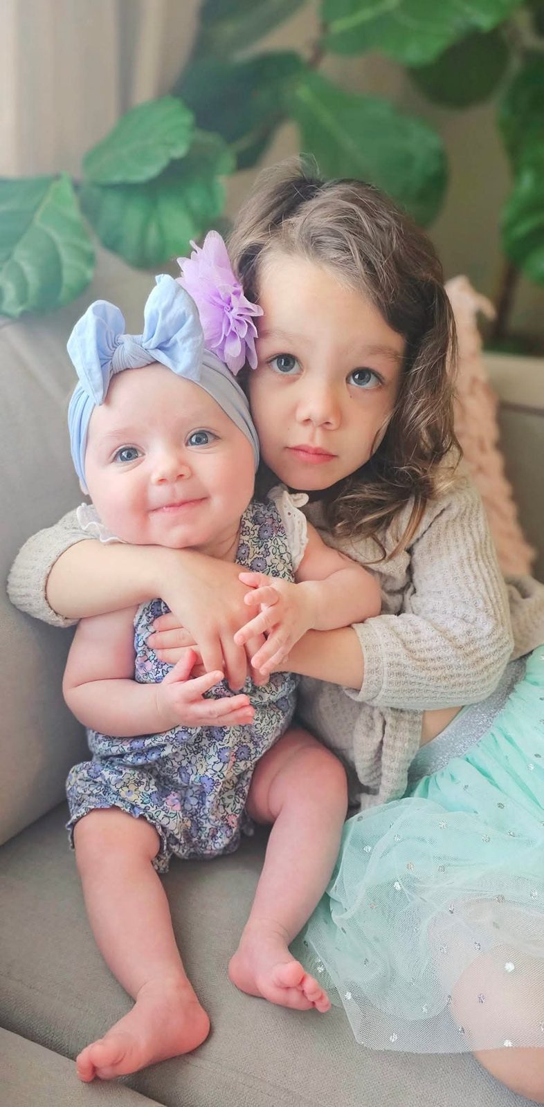 Big sister hugging her baby sister on the couch