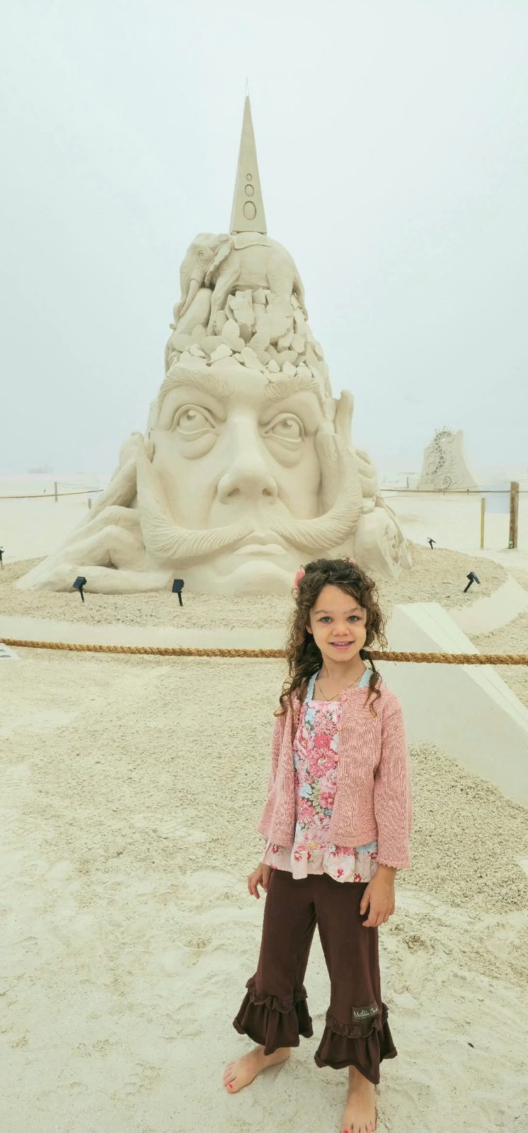 Girl in a pink cardigan in front of a giant sand sculpture
