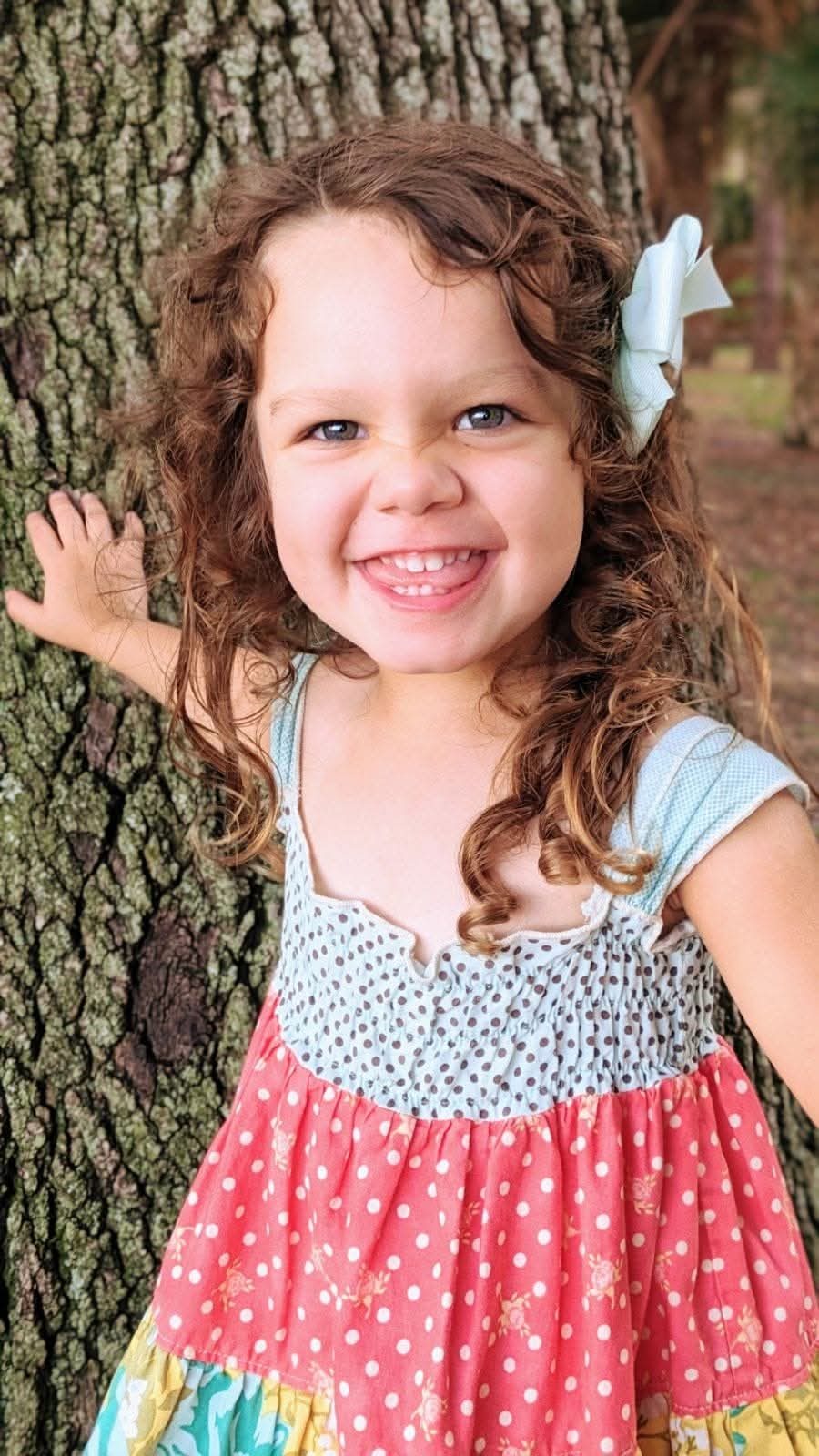 Curly-haired girl grinning beside a tree