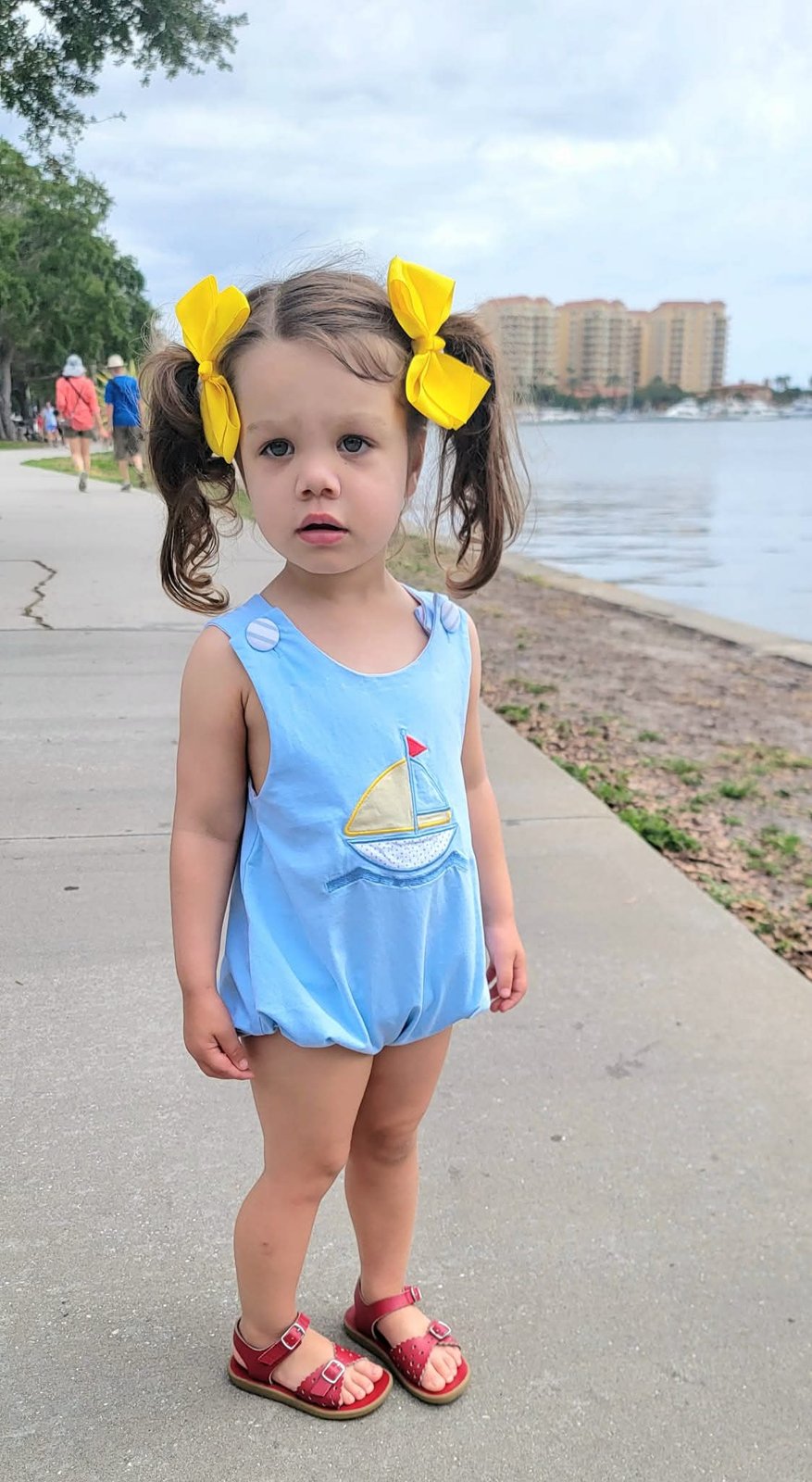 Toddler in a sailboat romper by the bay