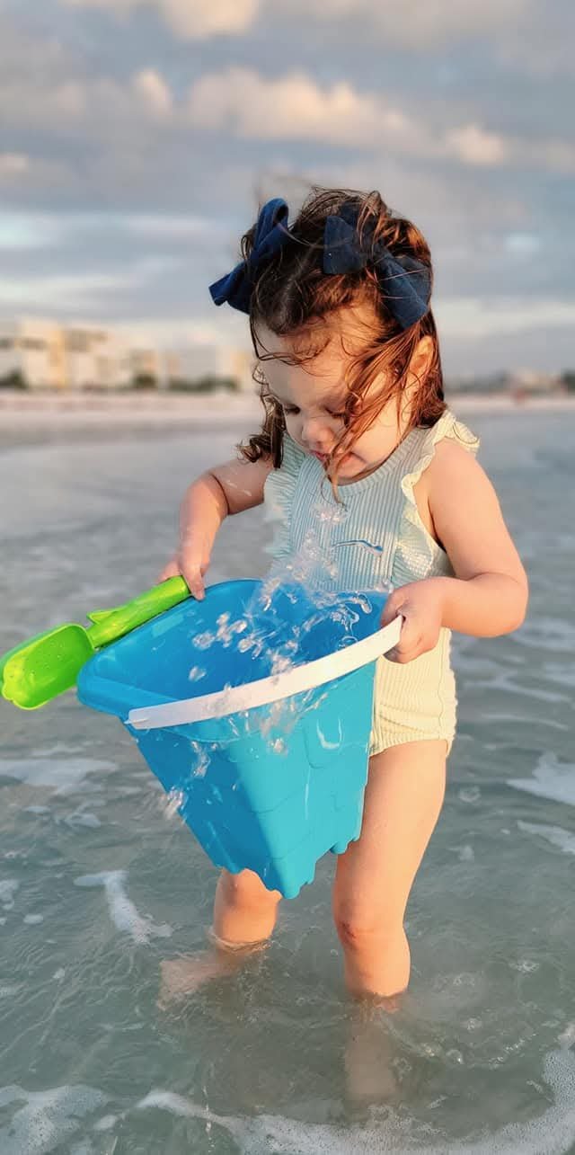 Toddler pouring a bucket of water in the surf