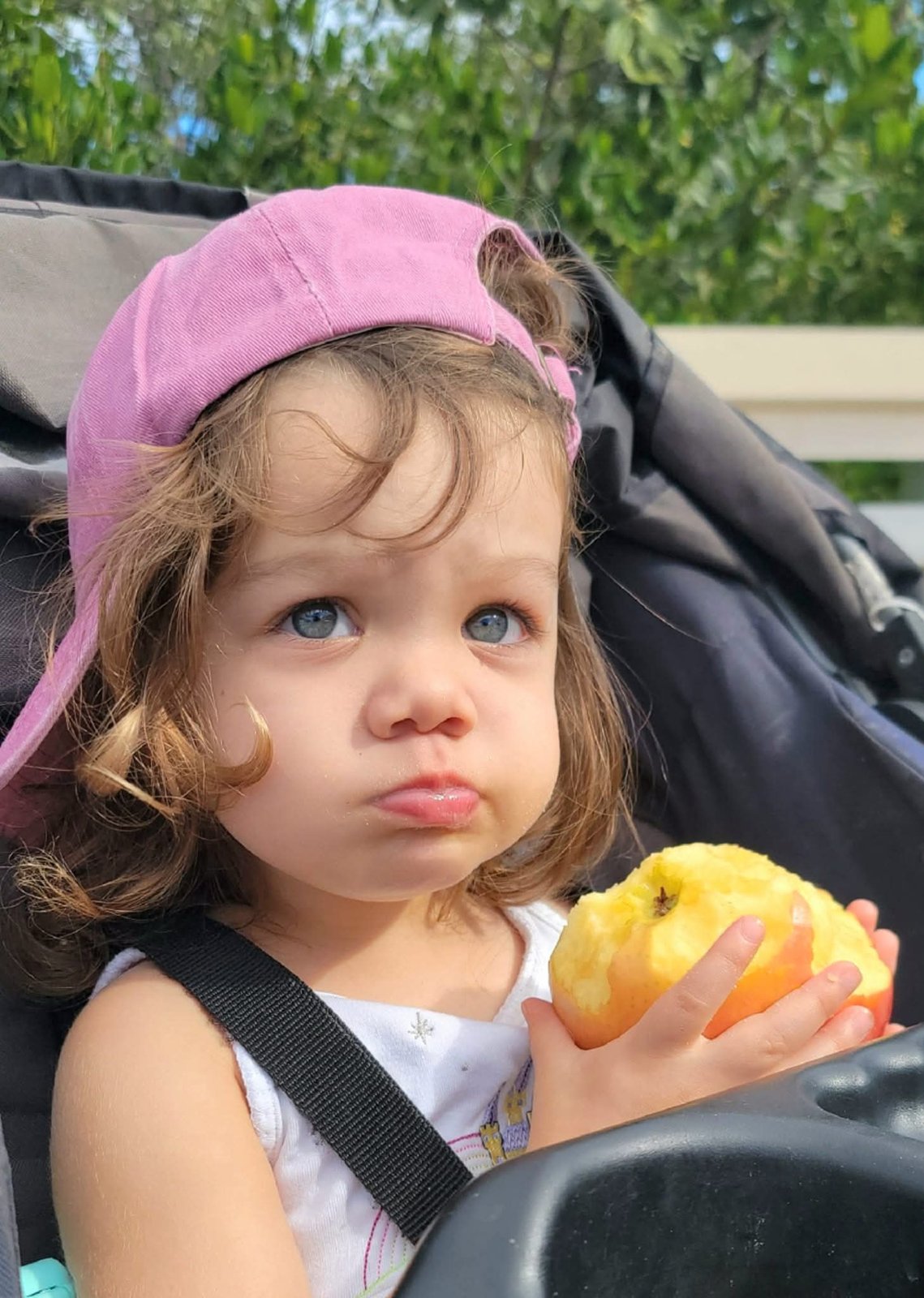Toddler in a pink cap eating an apple