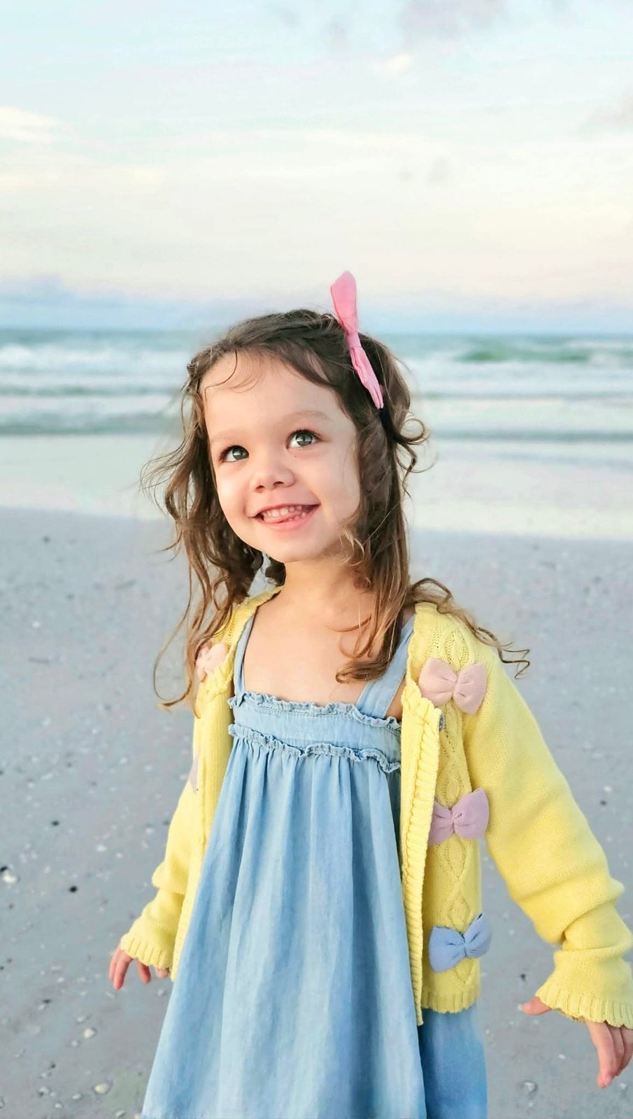 Girl in a yellow cardigan smiling on the beach