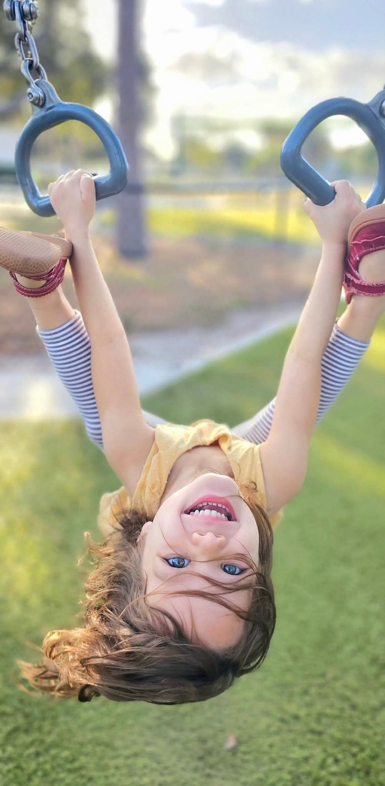 Girl hanging upside down from playground rings