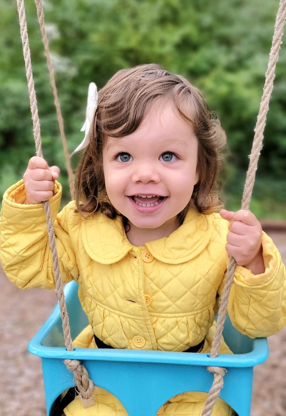 Toddler in a yellow coat smiling on a swing