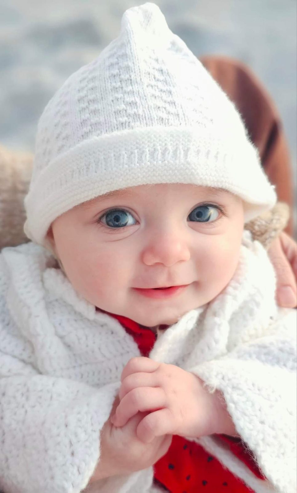 Smiling baby in a white knit hat and blanket