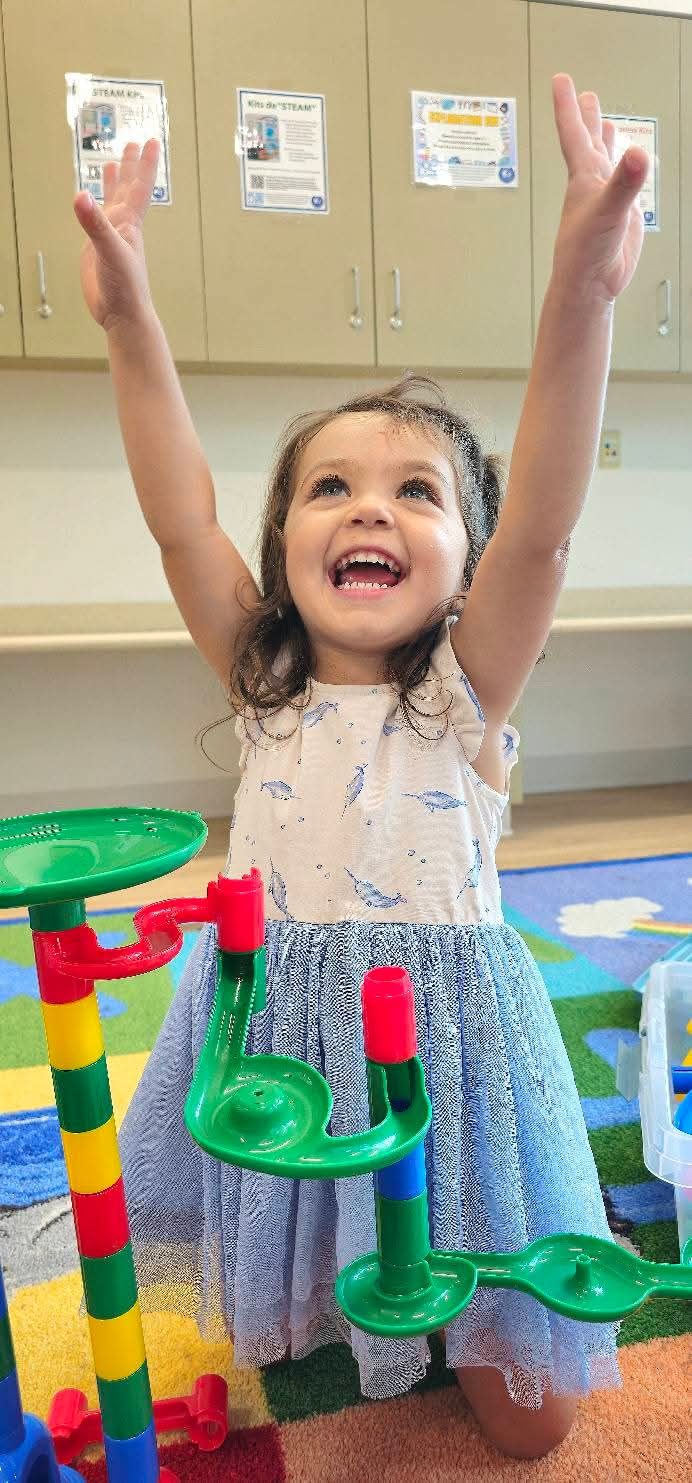 Girl cheering with arms raised by a marble run