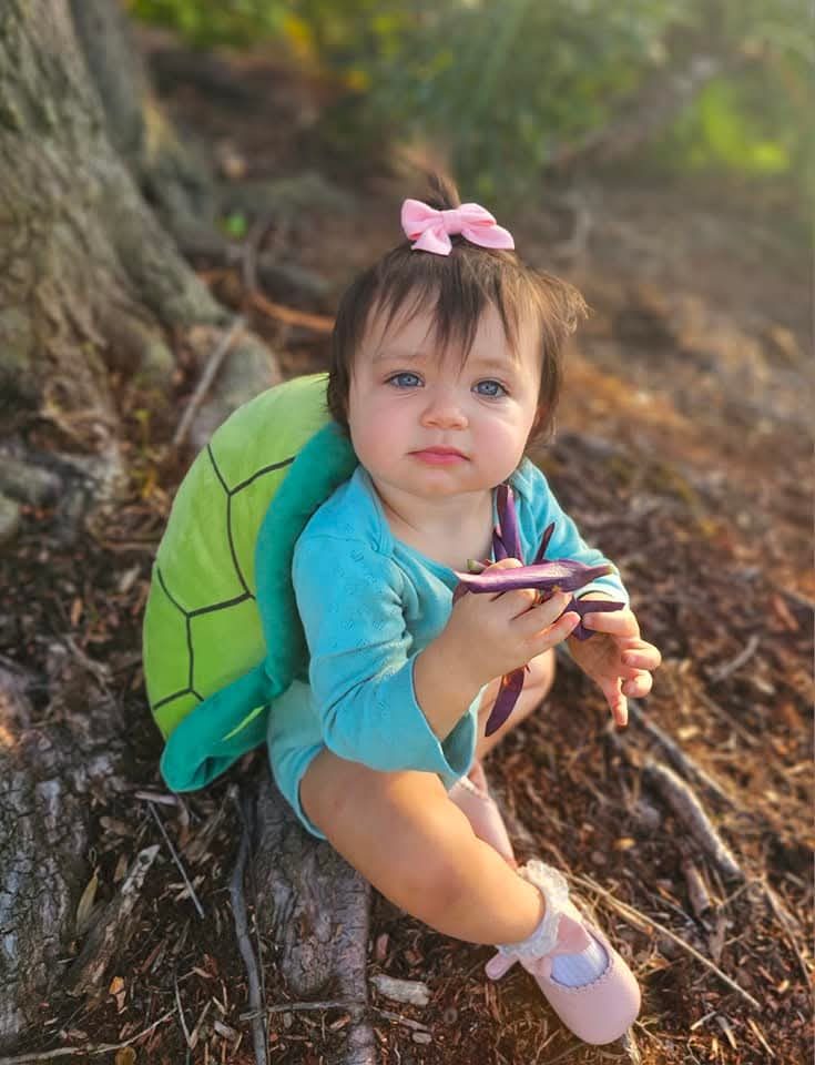 Baby in a turtle costume under a tree