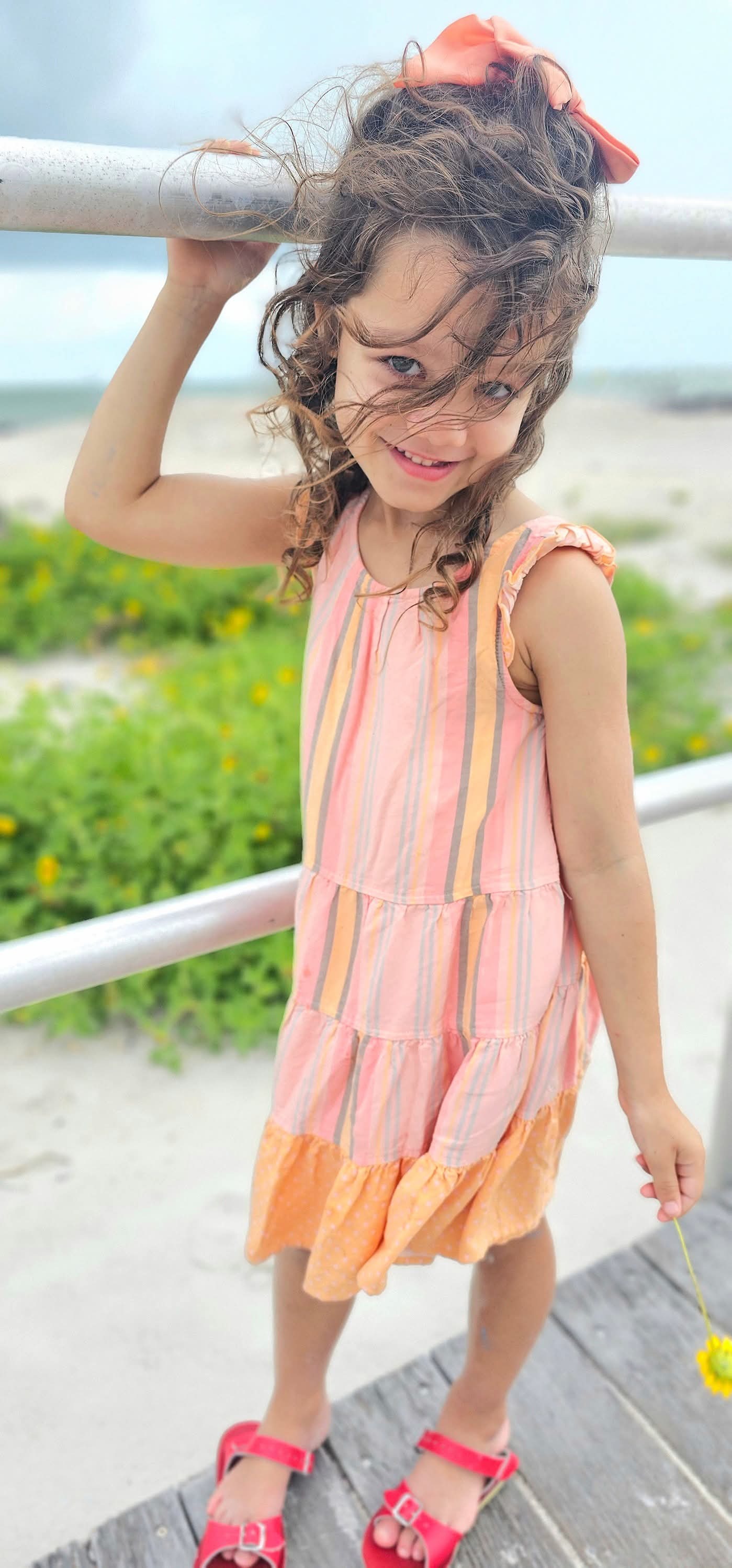 Girl with windswept curls across her face, holding a beach railing